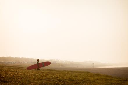 写真：サーブボードをもって浜辺をあるくサーファー